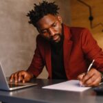 Um homem negro focado de terno está trabalhando em um laptop.